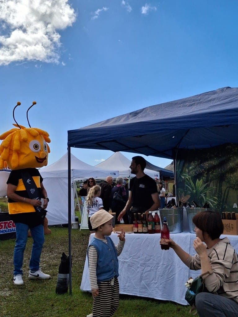 Aroā founder and the bee mascot smiling at the camera at the stand